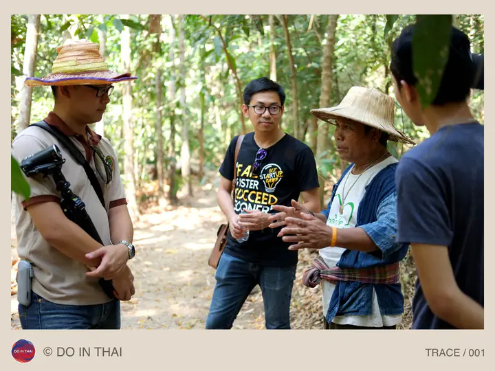 A person in a straw hat gestures to a small group listening among trees.
