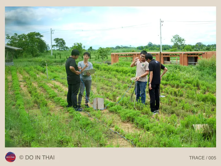 A small group talks in a planted field with buildings behind them.