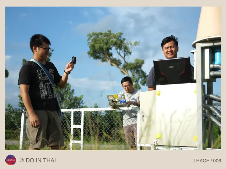 People use a phone and a laptop beside an outdoor equipment cabinet.