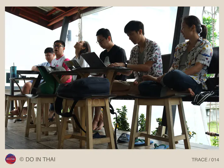 People use laptops at wooden tables in an open-sided space.