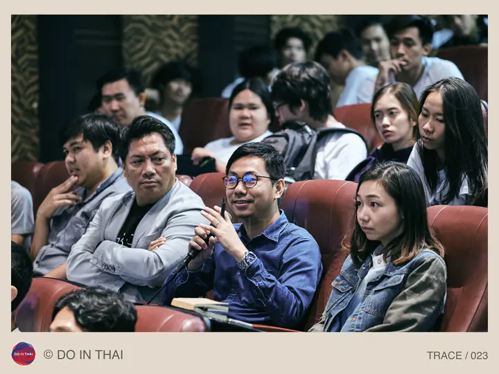 A person speaks into a microphone from a row of audience seats in an auditorium.