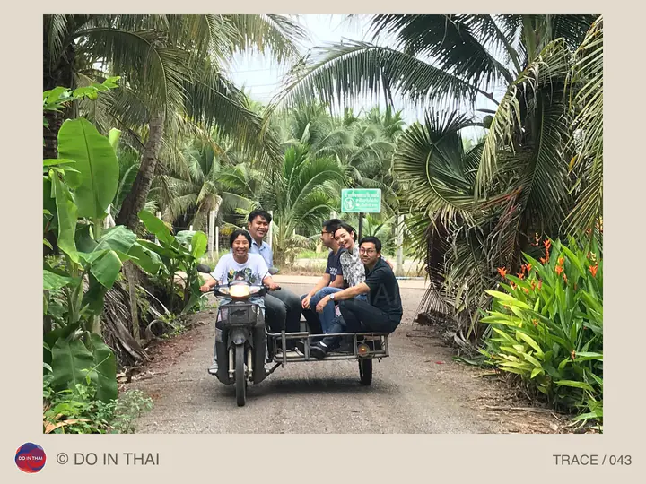 A group rides a motorcycle with a sidecar on a narrow path through coconut palms.