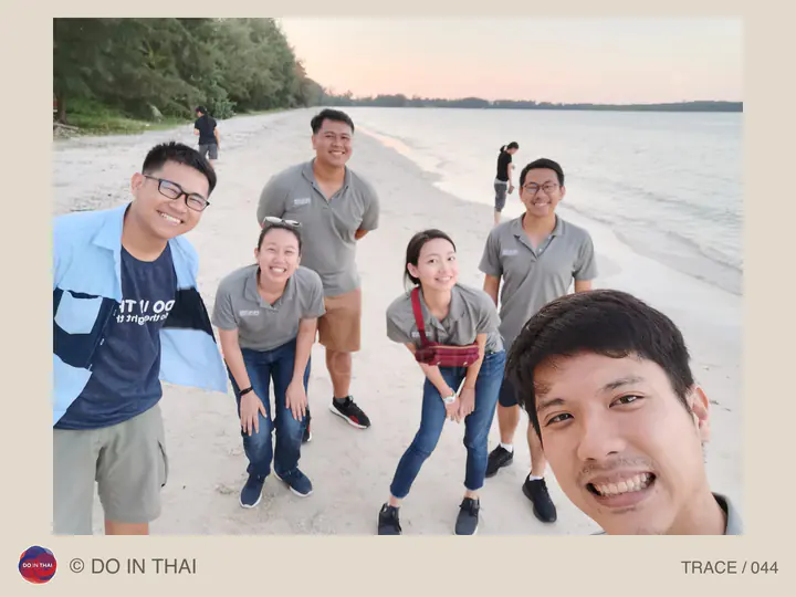 A team takes a selfie on a beach beside calm water under a pale sky.