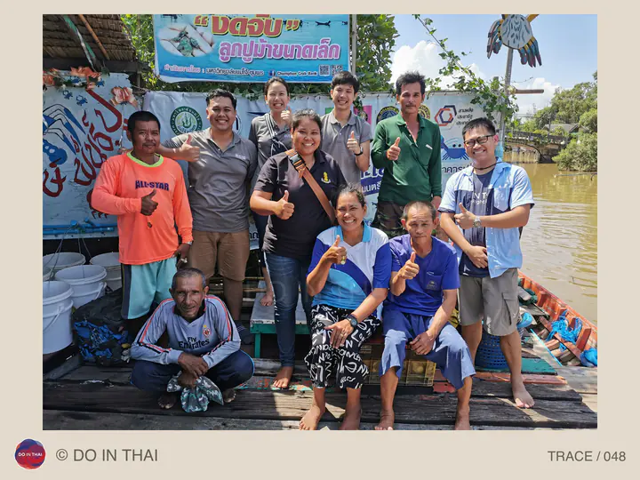 People of different ages pose on a wooden landing beside a canal and a food stall.